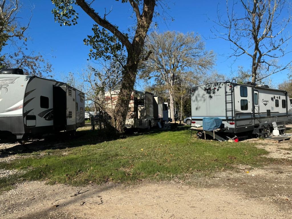 Row of travel trailers and fifth-wheels parked under bare trees at Sugar Land RV Park