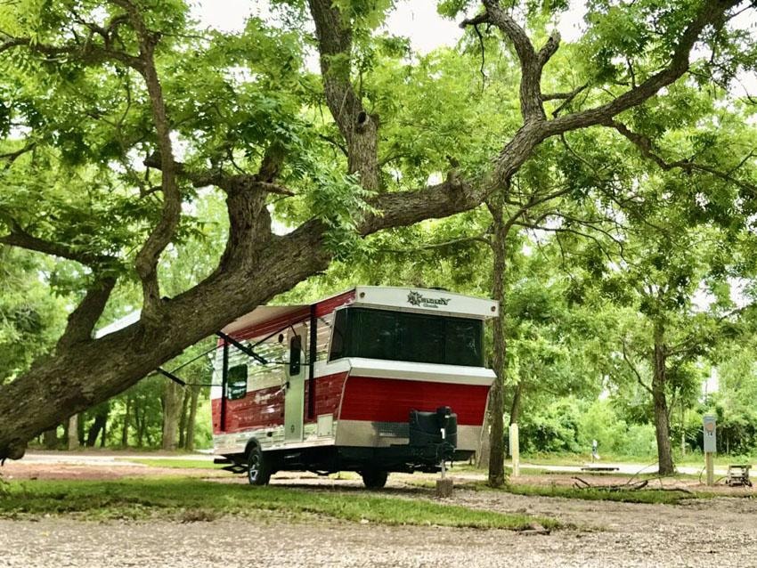 Red and white RV parked under large oak trees at Sugar Land RV Park