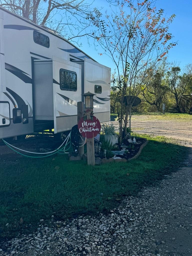 Fifth-wheel RV with Merry Christmas sign and landscaped garden at Sugar Land RV Park