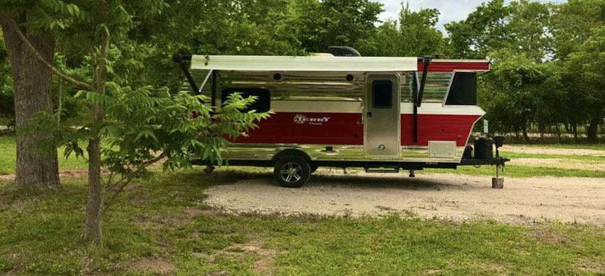 Red and silver Terry travel trailer with awning parked under trees at Sugar Land RV Park